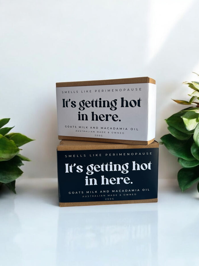 Two bars of soap with packaging that reads 'It's getting hot in here.' One bar is on top of the other, with a white background and green plants in the corners.